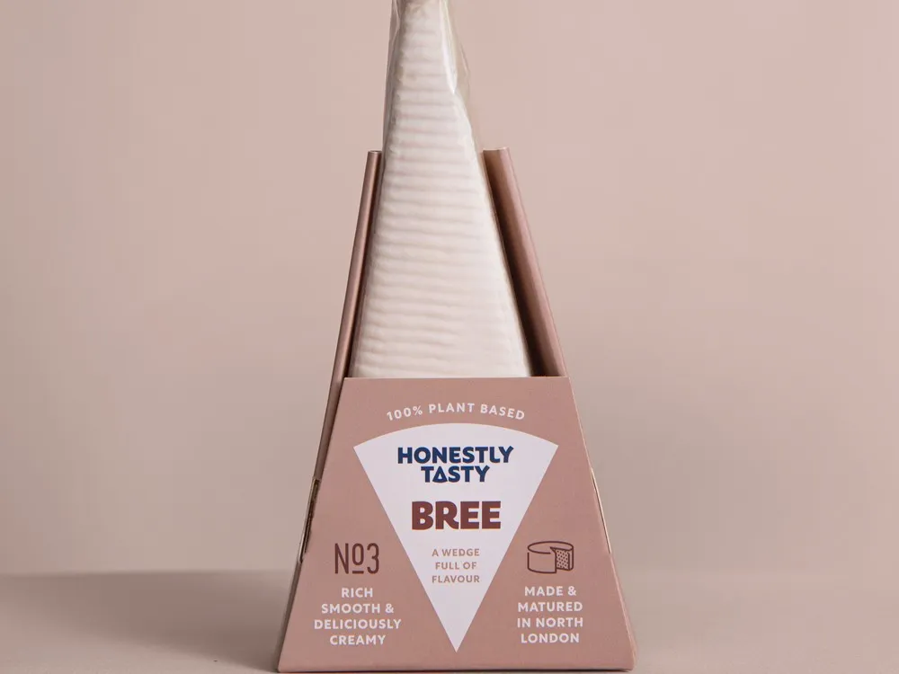 A packet of Bree vegan cheese, wrapped in a white sheet, is set against a beige background.