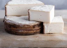 A Plancherin d'Arêches cheese wheel, wrapped in a band of sapwood and cut into triangular pieces, reveals its smooth, white interior, resting on a wooden surface