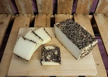 A block of Hotspur cheese, coated in cracked black pepper, is arranged on a wooden cutting board alongside several slices