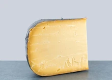 A wedge of Old Dutch Gouda cheese with a deep golden yellow color, displayed against a grey background