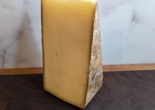 A wedge of Alpha Tolman cheese, showcasing its yellow interior and natural rind, rests on a wooden surface