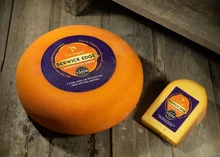 A wheel of Berwick Edge cheese, with its plastic rind, sits next to a slice of the cheese on a wooden surface