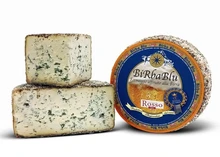 A wheel of Birba Blu cheese with its label, accompanied by a stacked half-cut and a slice, all set against a white background