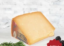 A slice of Gruyère cheese displayed on a wooden surface, accompanied by fresh herbs and berries