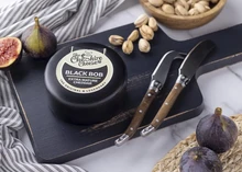 Black Bob Extra Mature Cheddar, encased in black wax and labeled, sits on a wooden cutting board alongside a knife, fresh figs, and nuts.