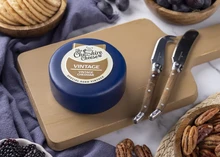 A wax-coated Vintage Special Aged Mature Cheddar with a label sits on a wooden board, surrounded by cheese knives, fresh fruits, nuts, berries, and cracker