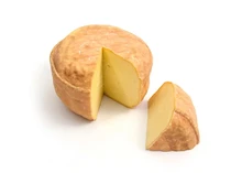 A slice and a small disc of Celtic Promise, both showcase orange rind and soft, yellow interior, set against a white background
