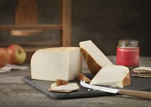 Large slices of Chesterwood cheese, apples, crackers and a knife, sits on a black marble slab, all arranged on a wooden surface