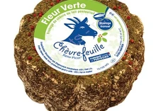 A labeled Chevrefeuille cheese, adorned with pink peppercorns and herbs, is set against a white background.