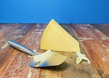 A slice of Cornish Kern cheese with a cheese slicer placed on a wooden surface