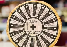 A wheel of Crémeux des Alpes Signature cheese featuring a label that provides detailed information about the cheese