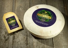 A wheel of Cuddy's Cave cheese, sits next to a slice of the cheese on a wooden surface