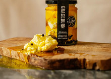 Graceburn cheese, dipped in oil with garlic and herbs and packed in a glass bottle, is accompanied by portions of the cheese and oil on a wooden surface