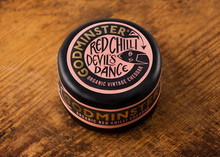 Godminster Red Chilli Devil's Dance Organic Vintage Cheddar enrobed in black wax to protect it, rests on wooden surface