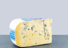 A slice of Dutch Blue cheese, showcasing blue veins and a creamy, smooth interior, rests on a grey surface