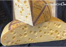 An Emmental cheese wheel, cut in half to reveal its large holes, with a slice of Emmental cheese placed on top of the cut portion