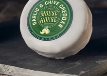 A wax-coated Mouse House Garlic & Chive Cheddar rests on a sleek black surface