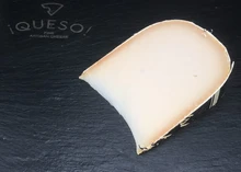 A wedge of Goat Gouda cheese sits on a black surface