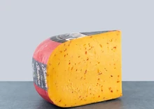 A slice of Hot Chili cheese wheel, showing a creamy interior with red chili pepper flecks