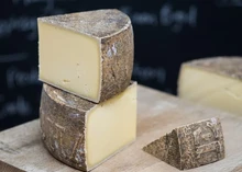 Triangular pieces of Le Maréchal cheese, stacked on a wooden surface, reveal a dark brown rind and a smooth, buttery interior