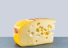 A slice of a Maasdam cheese with a bright yellow rind and a pale yellow interior with eyes (holes)