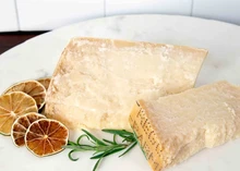 Slices of Cravero Parmigiano Reggiano arranged on a white plate, accompanied by dried lemon slices and fresh herbs