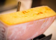 A partially sliced Raclette cheese revealing its soft interior, paired with a cheese cutting tool