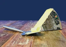 A slice of Affineur Walo Rotwein Sennechäs cheese, with a cheese slicer beside it, rests on a wooden surface