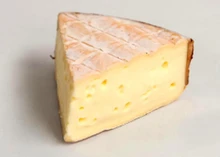 A slice of Rollright cheese, showcasing its peachy-pink rind and spoonable, silky paste.