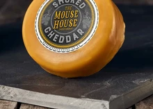 A wax-coated Mouse House Smoked Cheddar is placed on a wooden surface