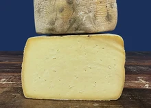 Slices of Swaledale cheese are stacked on a wooden surface, set against a dark blue background