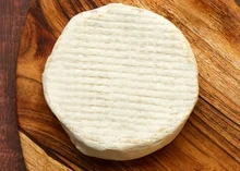 A disc of Truffle Camemvert, a plant-based Camembert alternative with a white bloomy rind, rests on a wooden surface
