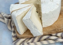 A round-shaped White Nancy cheese and slices showing creamy white bloomy rind sits on a wooden surface