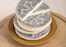 Fromage Cathare cheese discs are stacked on a wooden plate, highlighting their ash-coated exteriors and smooth, ivory interiors