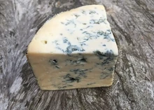 A triangular slice of Cashel Blue cheese, showcasing its creamy paste with prominent blue veins, rests on a wooden surface