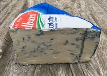 A triangular piece of Dolcelatte cheese, featuring blue veins and a crumbly interior, along with a blue wrapper, rests on a wooden surface