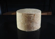A cylindrical-shaped Traditional Ayrshire Dunlop PGI cheese, wrapped in cloth, rests on a black surface
