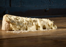 A slice of Gorgonzola Dolce rests on a wooden surface, showcasing its luxurious, creamy, spreadable texture with delicate blue and green veining