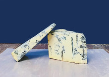 Slices of Gorgonzola Piccante DOP cheese, with its blue veins on a creamy interior, are arranged on butter paper on a wooden surface