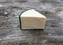 A slice of Mature Yorkshire Wensleydale cheese, with a pale yellow interior and green wax rind, rests on a wooden surface