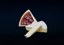 Triangular pieces of Howgate Brie Cheese, displaying a bloomy rind and creamy interior, with a label, set against a black background