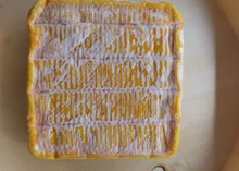 A square-shaped Minger cheese with its orange rind, placed on beige paper