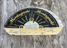 A halved wheel of Montagnolo cheese, labeled on top, reveals its creamy blue-veined interior, resting on a rustic wooden surface