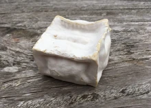 A square-shaped Pavé d'Affinois with its ivory bloomy rind rests on a wooden surface