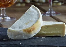 A wheel of Reblochon cheese, cut in half to reveal its smooth interior and mold-covered rind, rests on a black marble