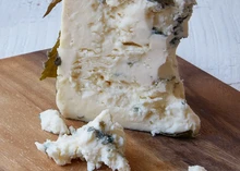 A piece of Rogue River Blue cheese, revealing its smooth texture and intricate blue veins, with a portion of Syrah grape leaves resting on a wooden surface