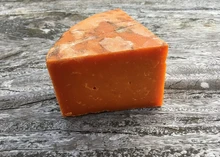 A wedge of Ruthland Red, showing distinct orange color from annatto rests on a wooden surface