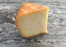 A slice of Lyburn Lightly Oak Smoked cheese, featuring a golden-brown rind and a smooth interior, rests on a wooden board
