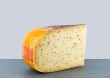 A slice of Cumin Gouda, its smooth texture and creamy consistency accented by cumin seeds, set against a grey background
