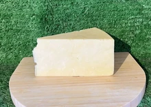 A wedge of White Stilton PDO cheese rests on a wooden disc, showcasing its crumbly texture
